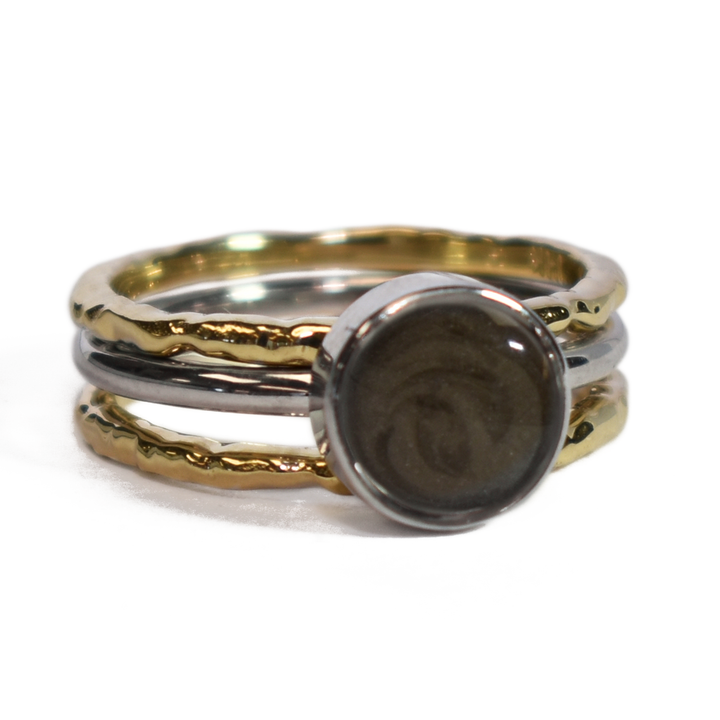 This photo shows a stacking cremation ring set from close by me jewelry from the front and at a slight angle. The Cremains Ring is an 8mm Circle Stacking Ring in Sterling Silver between two 14K Yellow Gold Textured Companion Rings