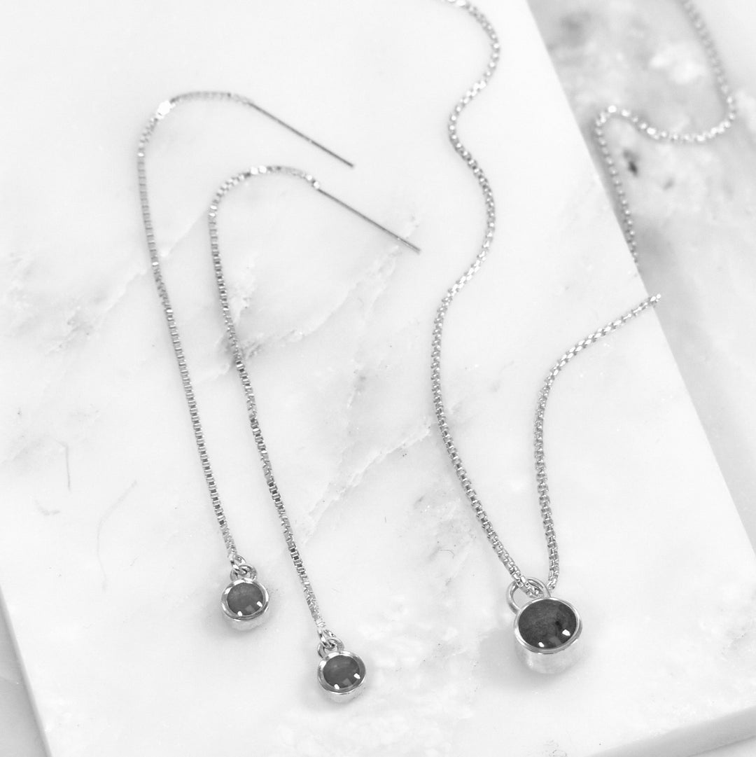 Pictured here are both the Bilateral Cremated Remains Necklace and Chain Cremation Earrings designed by close by me jewelry lying flat against a piece of white marble