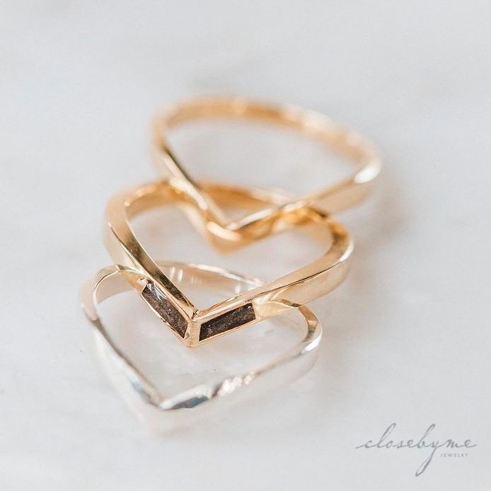 This photo shows Chevron Ashes and Companion Ring designs by close by me jewelry in 14K Yellow Gold and Sterling Silver spread out on a white background