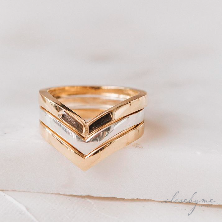 This is a picture showing mixed metal Chevron Cremains and Companion Rings by close by me jewelry stacked together on a flat piece of white paper