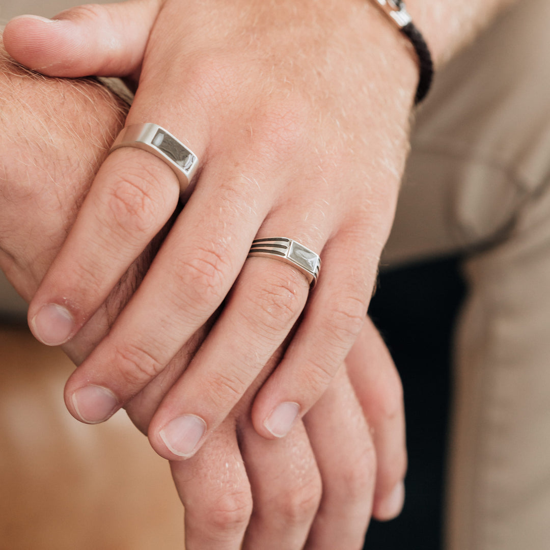 side angle of male hand wearing close by me's classic band cremation ring on index finger and ridged band rectangle signet cremation ring on ring finger