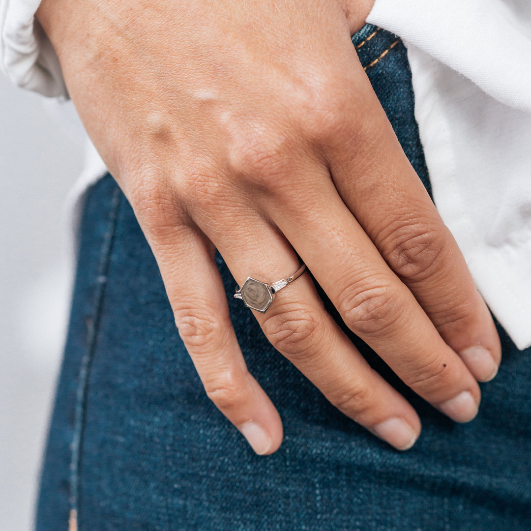 Pictured here is a model wearing close by me jewelry's 14K White Gold Hexagon White Baguette Diamond Band Cremation Ring in 14K White Gold. Her thumb is hooked inside of the pocket of her blue jeans and the tail of her white shirt hangs next to her hand.