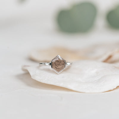  This photo shows close by me jewelry's Hexagon White Baguette Diamond Band Ashes Ring in 14K White Gold resting on a white shell with a blurred background