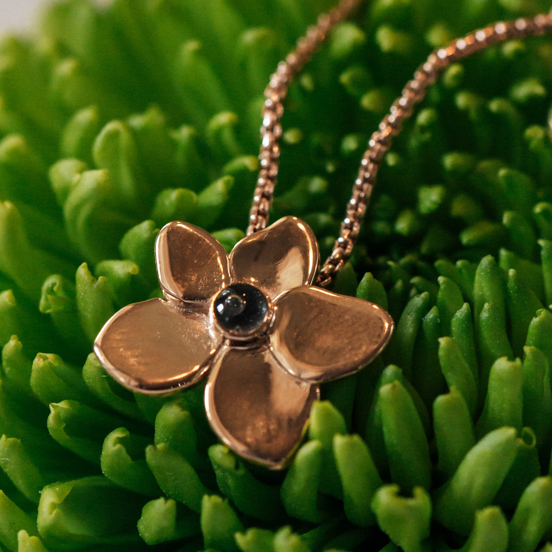 This photo shows the 14K Rose Gold Hydrangea Flower Cremains Necklace designed by close by me jewelry and lying flat against a green plant background