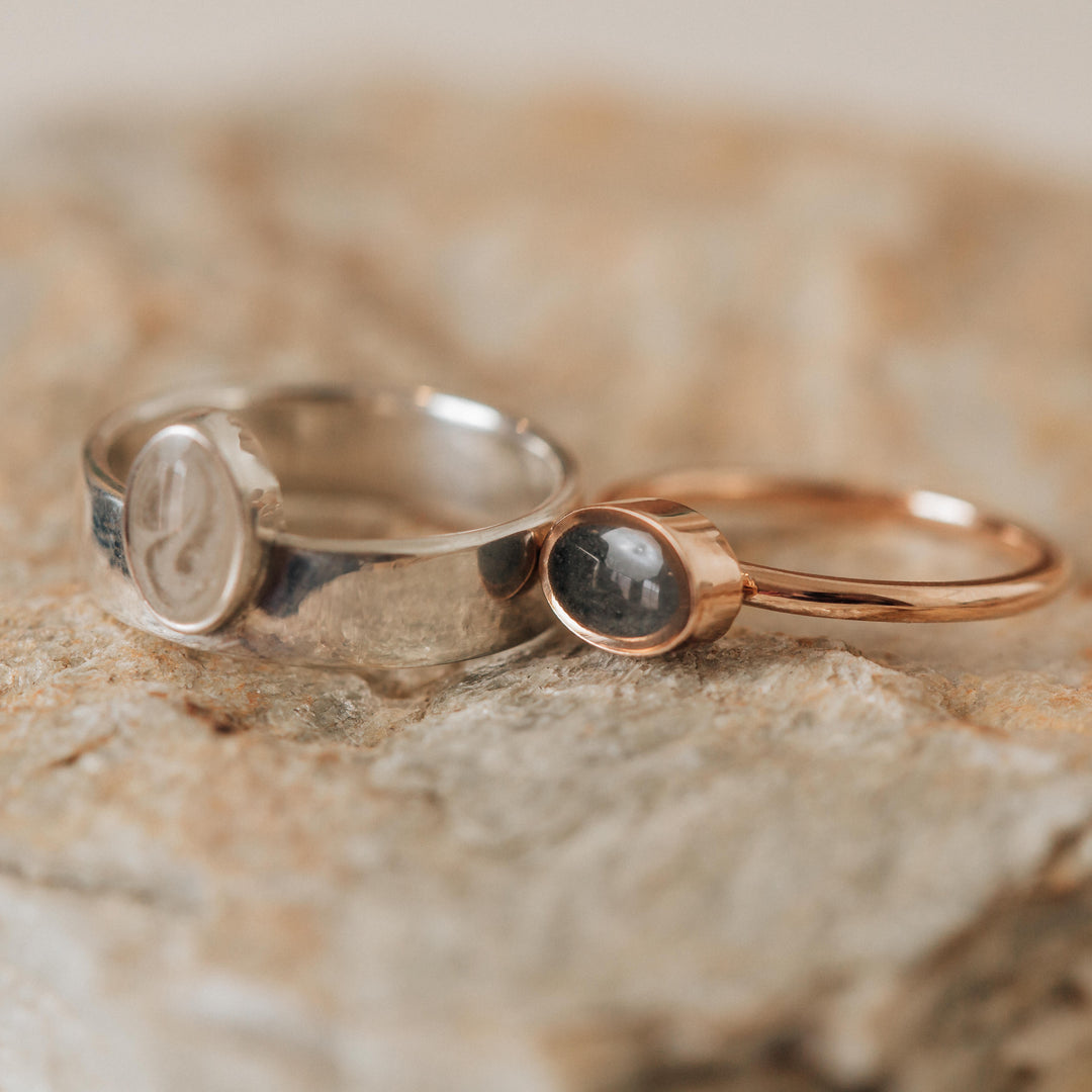 This photo shows several ashes ring designs by close by me jewelry; on the left of a Sterling Silver Ashes Ring is the 14K Rose Gold Lateral Oval Ashes Stacking Ring
