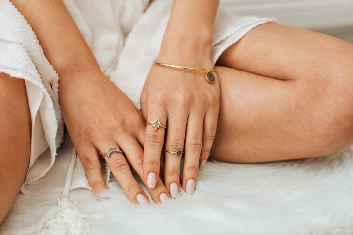 Pictured here are several pieces of cremation jewelry being worn by a light-skinned model. On the index finger of her left hand, she wears the 14K Yellow Gold North Star Ring.