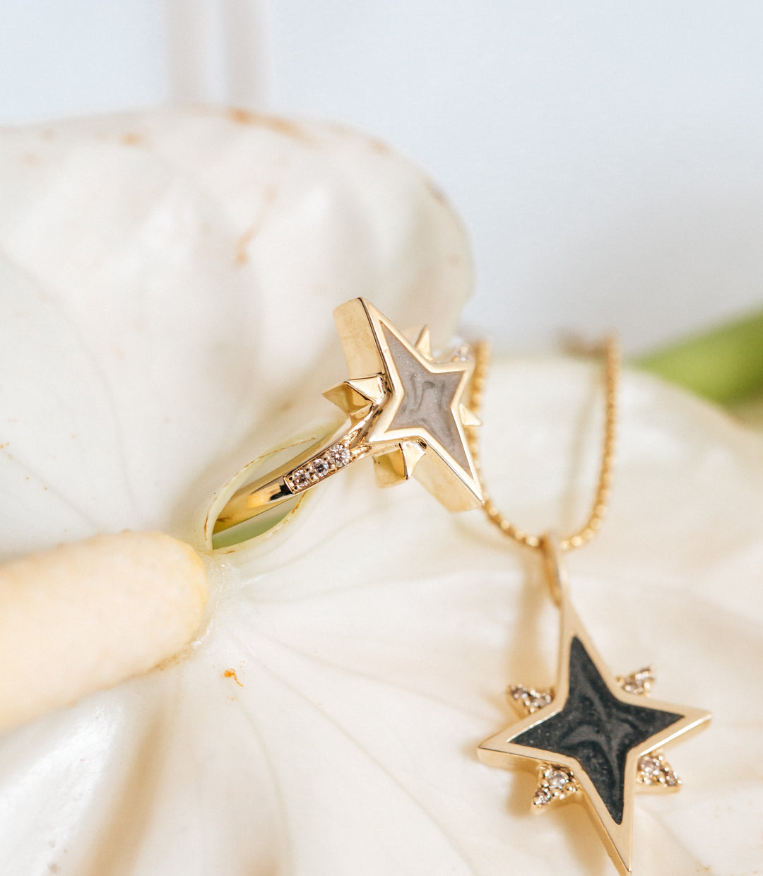 Pictured here are two of close by me jewelry's celestial cremation designs on the petal of a white Lily: the 14K Yellow Gold and Champagne Diamond North Star Ring and Pendant designs showing light and dark gray ashes settings