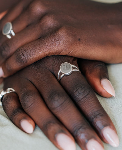 This photo shows a model's hands with several Sterling Silver Ashes Rings on her fingers. The Oval Split Shank Ashes Ring is on the index finger of her right hand