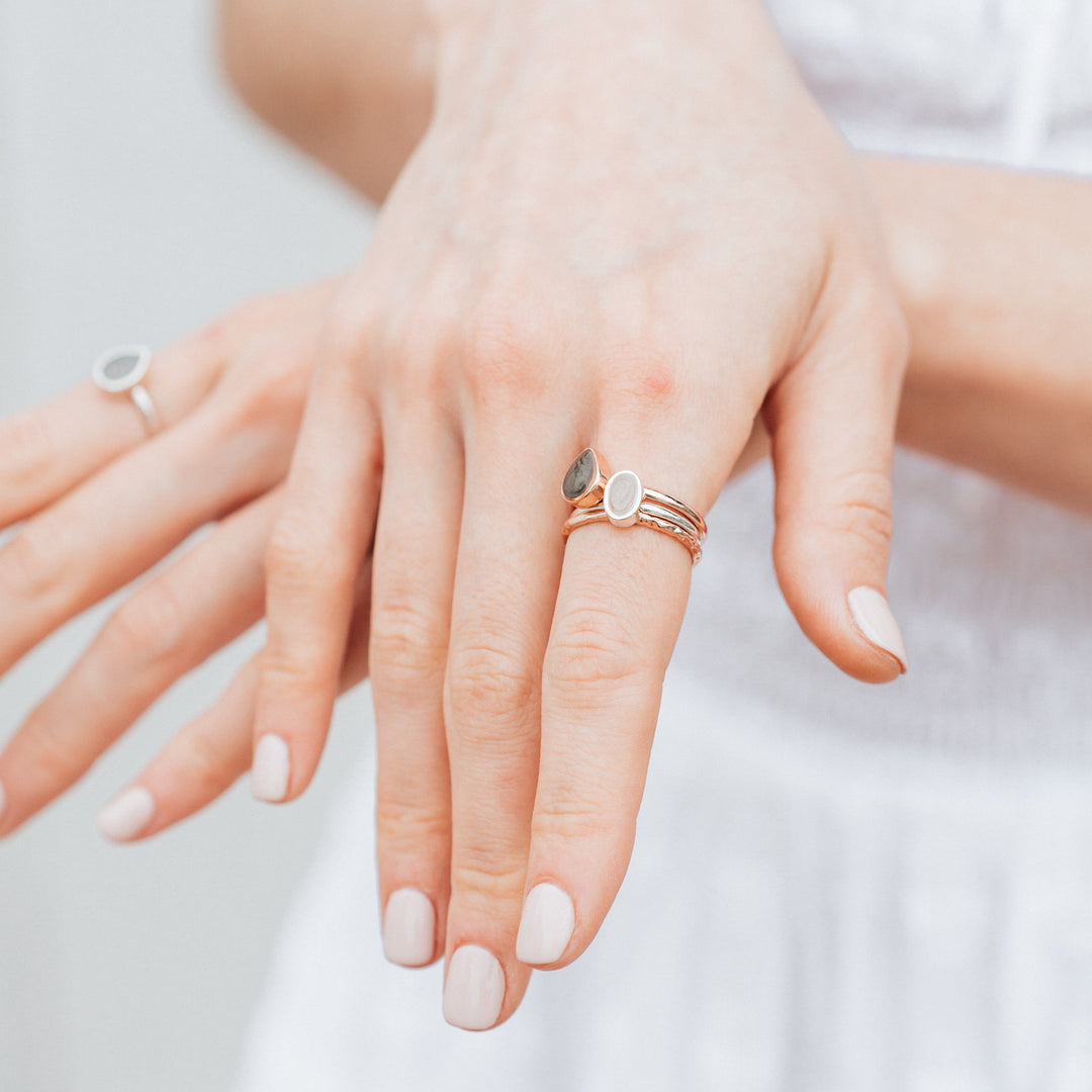 This photo shows a model wearing a mixed metal stacking ashes ring set designed by close by me jewelry; the Oval Stacking Cremains Ring in Sterling Silver is with two other stacking pieces on her index finger