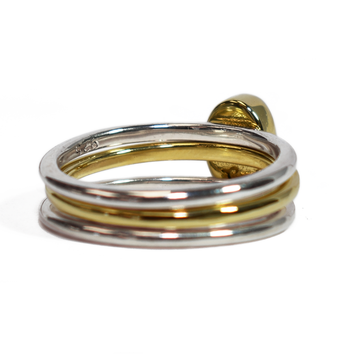 This photo shows the Mixed Metal Stacking Cremation Ring set designed by close by me jewelry with a 14K Yellow Gold Oval Stacking Ring with ashes between two Sterling Silver Smooth Companion Rings from the back at a slight angle