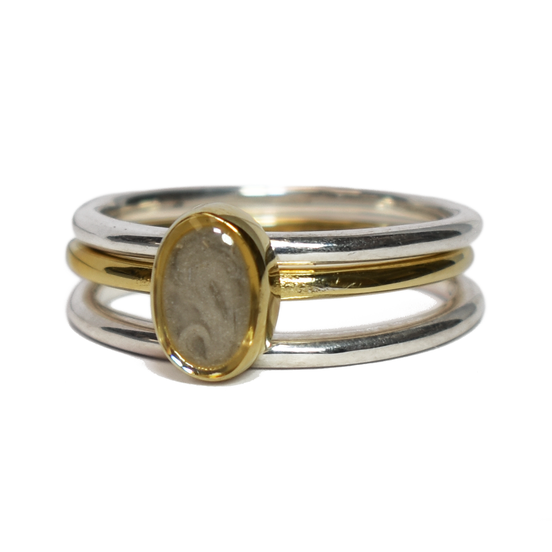 This photo shows the Mixed Metal Stacking Cremation Ring set designed by close by me jewelry with a 14K Yellow Gold Oval Stacking Ring with ashes between two Sterling Silver Smooth Companion Rings from the front but at a slight angle to the left