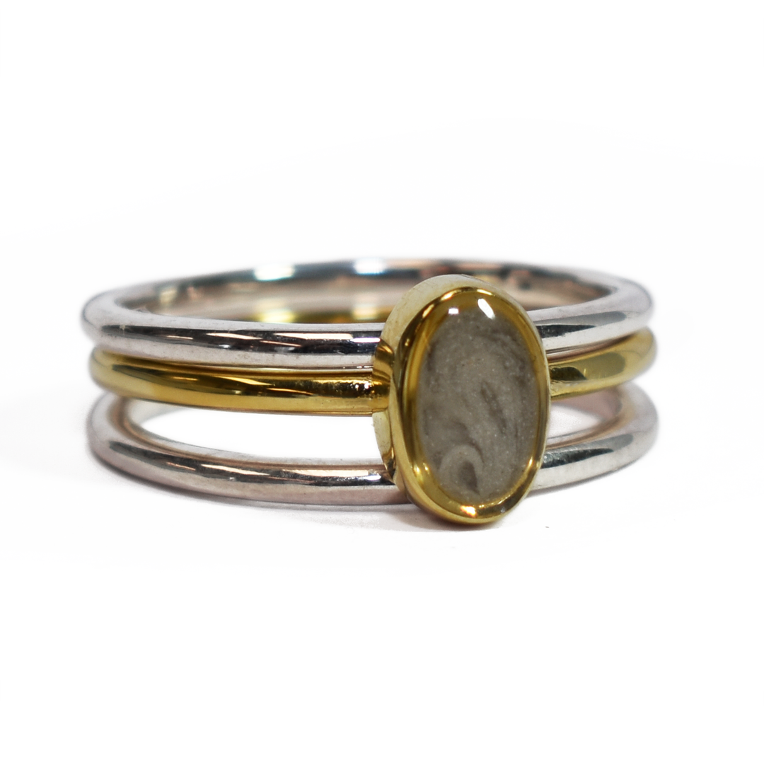 This photo shows the Mixed Metal Stacking Cremation Ring set designed by close by me jewelry with a 14K Yellow Gold Oval Stacking Ring with ashes between two Sterling Silver Smooth Companion Rings from the front at a slight angle to the right