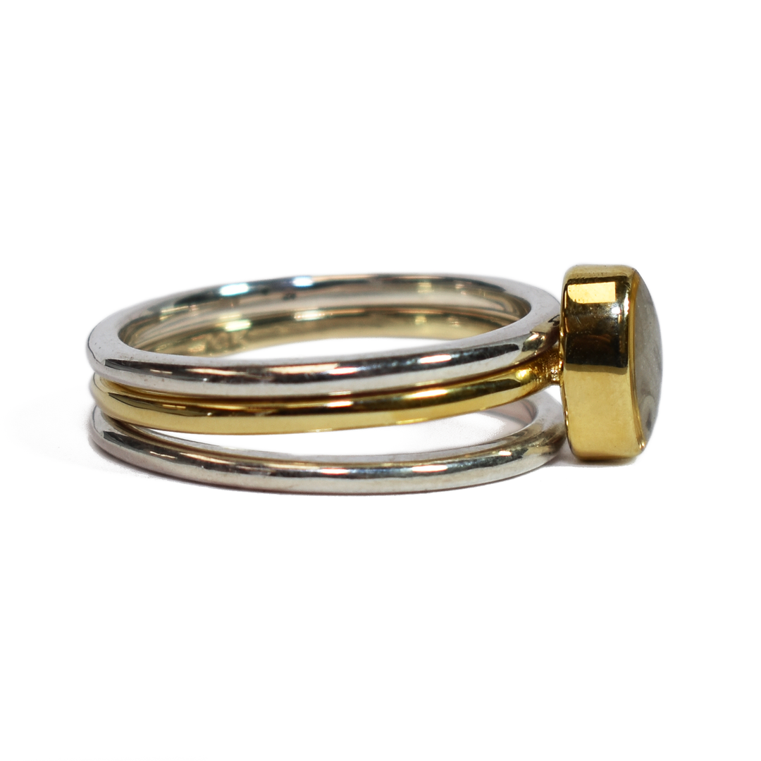 This photo shows the Mixed Metal Stacking Cremation Ring set designed by close by me jewelry with a 14K Yellow Gold Oval Stacking Ring with ashes between two Sterling Silver Smooth Companion Rings from the right side