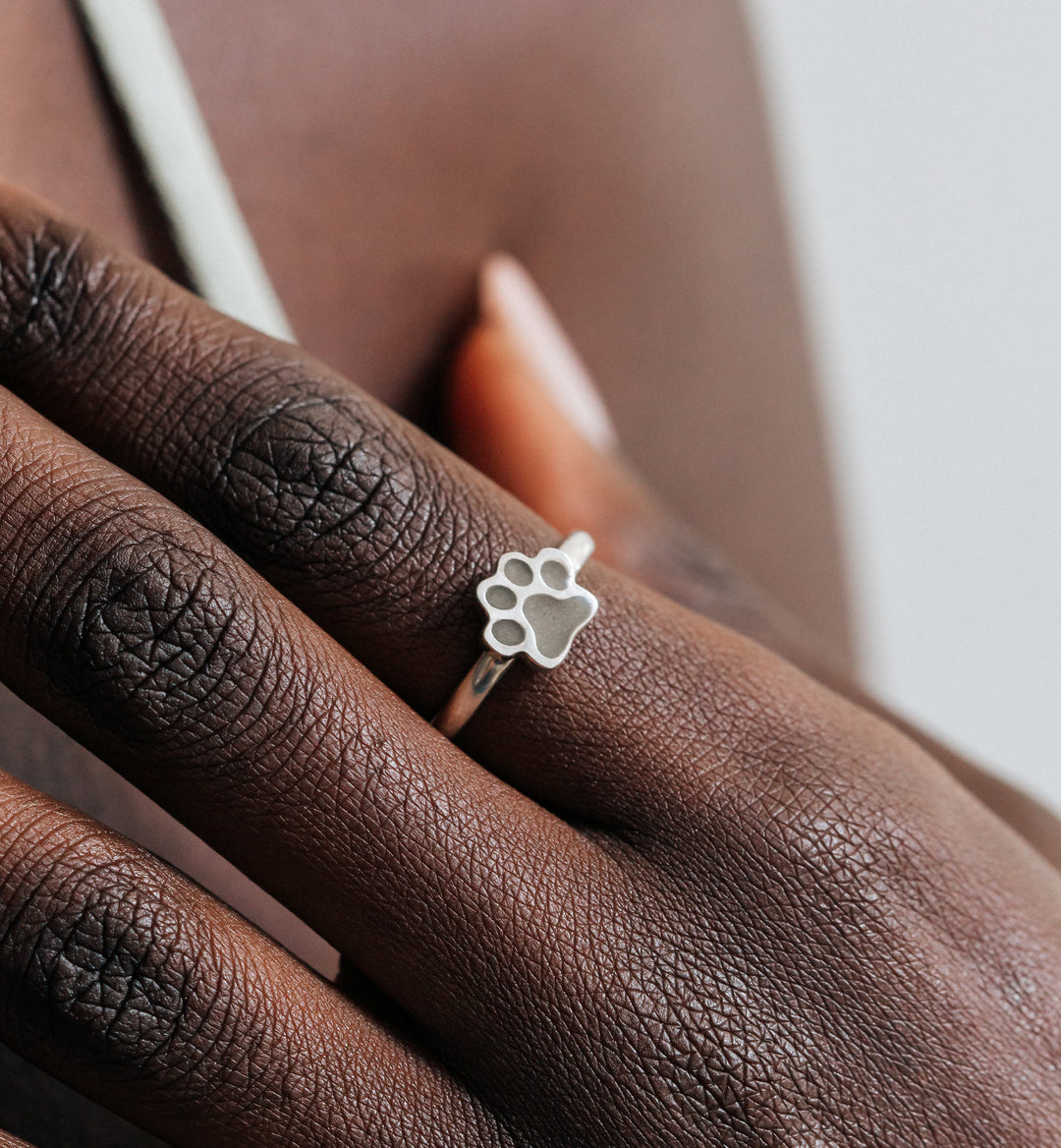 This photo shows a close up of a model wearing the Sterling Silver Paw Print Stacking Cremation Ring on her index finger