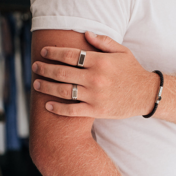 Pictured here is a male model wearing close by me jewelry's Men's Classic Band and Ridged Rectangle Signet Cremation Rings in Sterling Silver and the Leather Cord Cremation Bracelet