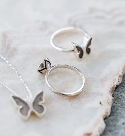 This photo shows several Sterling Silver Ashes jewelry pieces designed by close by me jewelry lying flat on a white stone. The Signature Lotus Stackable Band Cremains Ring can be seen from the back