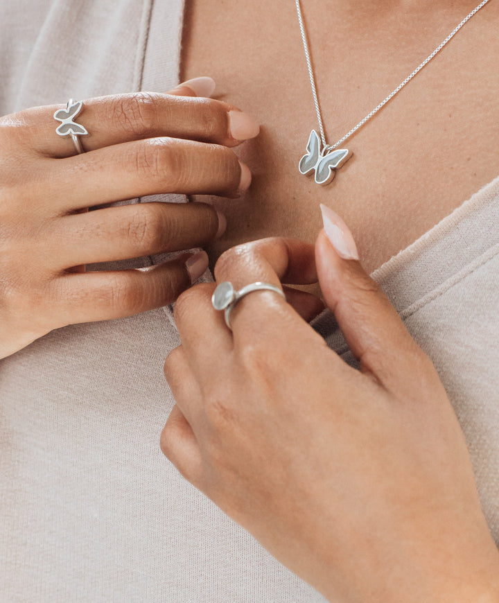 This photo shows close by me jewelry's Sterling Silver Signature Lotus Stackable Band Ring with ashes being worn by a model alongside the Butterfly Ashes Jewelry Collection