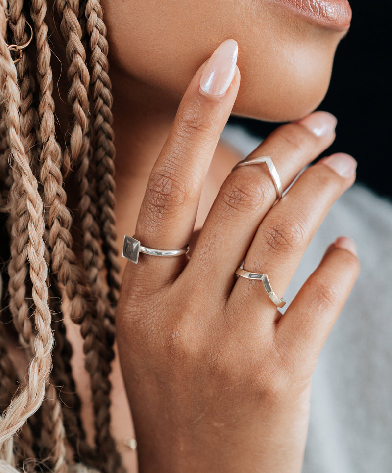 Pictured here are several cremation rings in Sterling Silver designed by close by me jewelry being worn by a model; on her index finger, she wears the Sterling Silver Signature Square Stackable Band Cremated Remains Ring