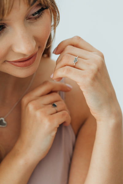 In this photo, a model wears the Small Heart Stacking Ashes Ring with cremated remains designed and set by close by jewelry on her ring finger
