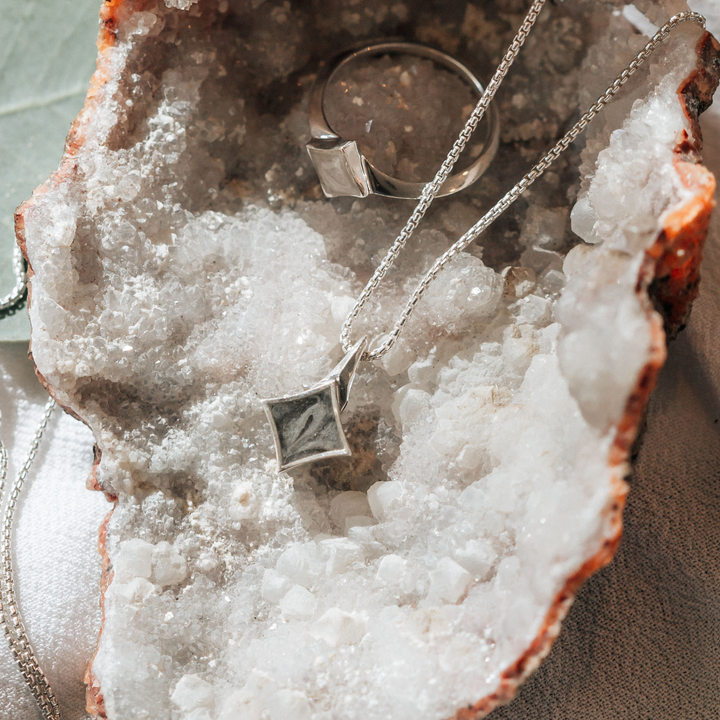 Pictured here are the Sterling Silver Luminary Cremains Ring and Necklace design by close by me jewelry lying flat inside of a crystal geode