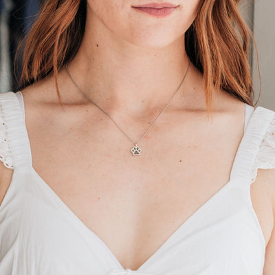 This photo shows close by me jewelry's Sterling Silver Small Paw Print Ashes Necklace around a model's neck