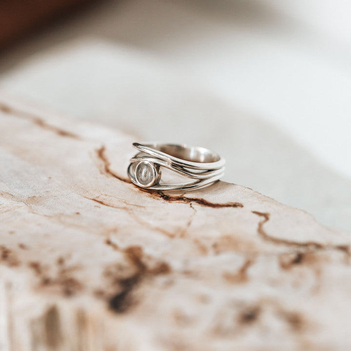 Pictured here is the Three Band Ashes Ring in Sterling Silver lying flat on a piece of light colored wood