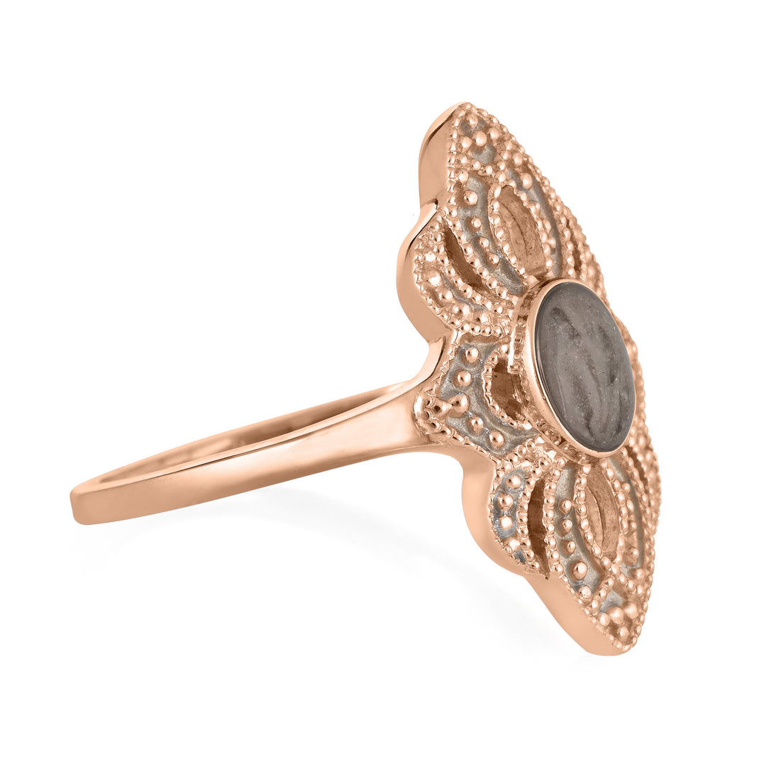 Pictured here is a close-up side view of Close By Me Jewelry's vintage-style World War II Cremation Ring in 14K Rose Gold set against a solid white background. This version of the ring features a smaller oval bezel containing solidified cremated remains. The ashes setting in this picture is dark gray in color and has a subtle swirl design.